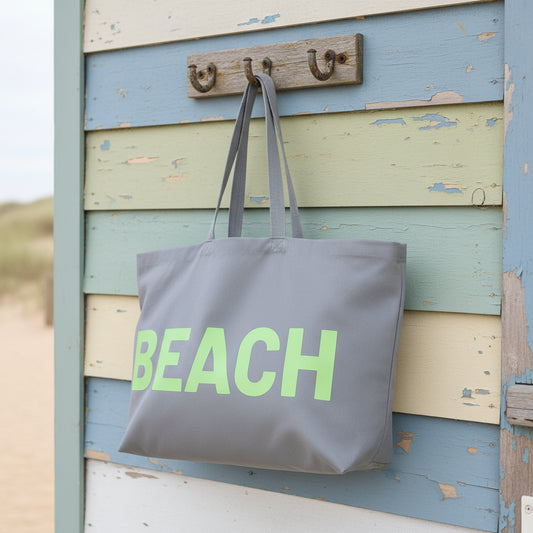 Gray tote bag with 'BEACH' in green on a beach hut background