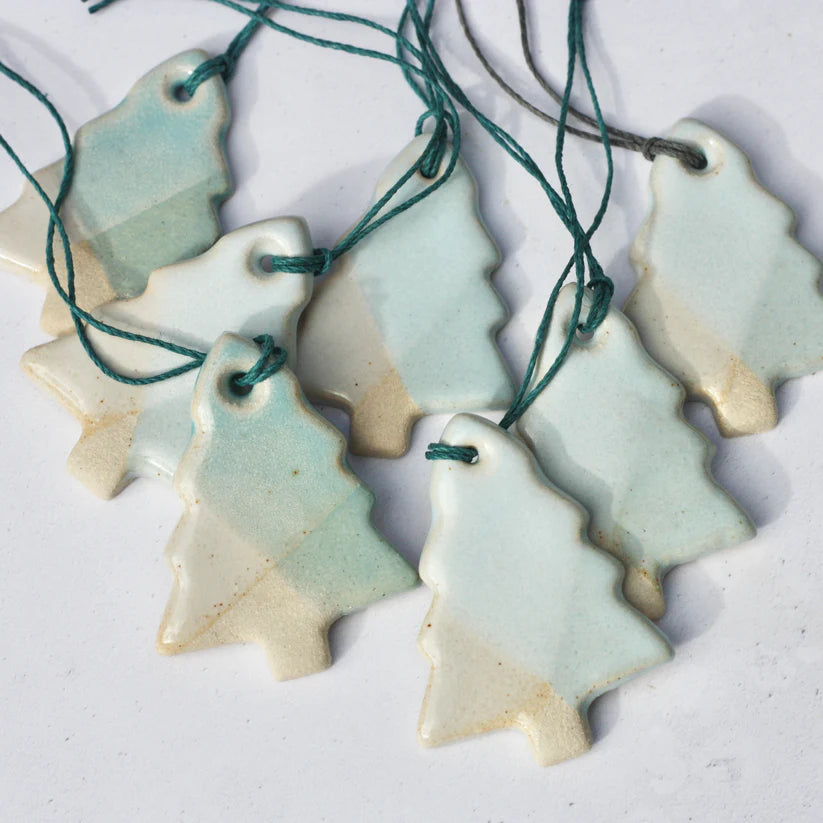 Collection of ceramic Christmas tree ornaments with green string on a white background