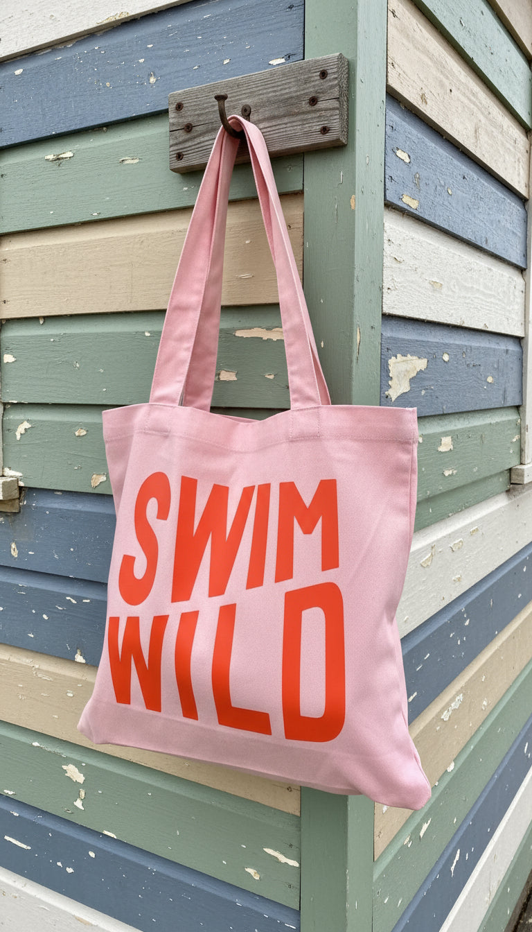 Pink tote bag with 'SWIM WILD' text on a dark background