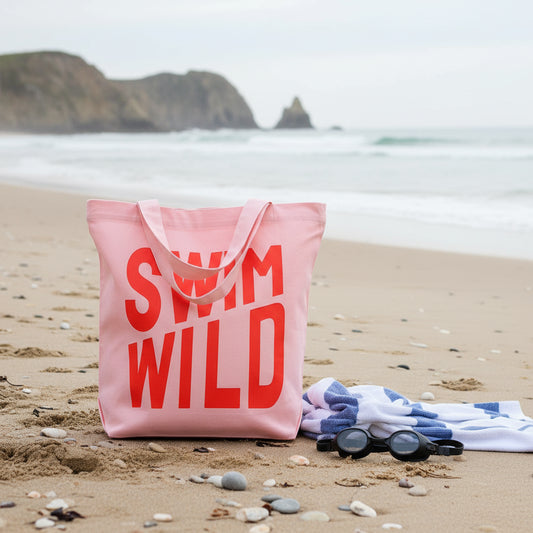 Person holding a pink tote bag with shocking pink 'SWIM WILD' text against a plain background