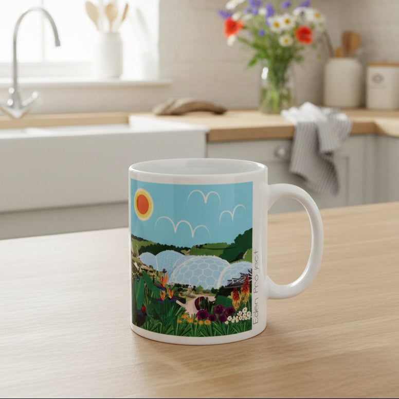A white ceramic mug featuring a colourful illustration of the eden project under a blue sky, set against a kitchen background.