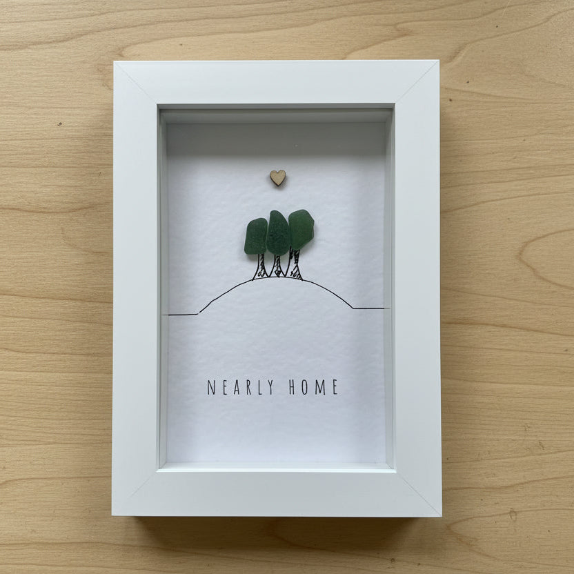 Decorative box with pebbles and 'NEARLY HOME' text on a wooden surface