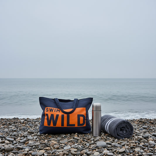 Wild Swim Navy Blue & Neon Orange Cotton Canvas Jumbo Bag sat on a beach with the sea behind it