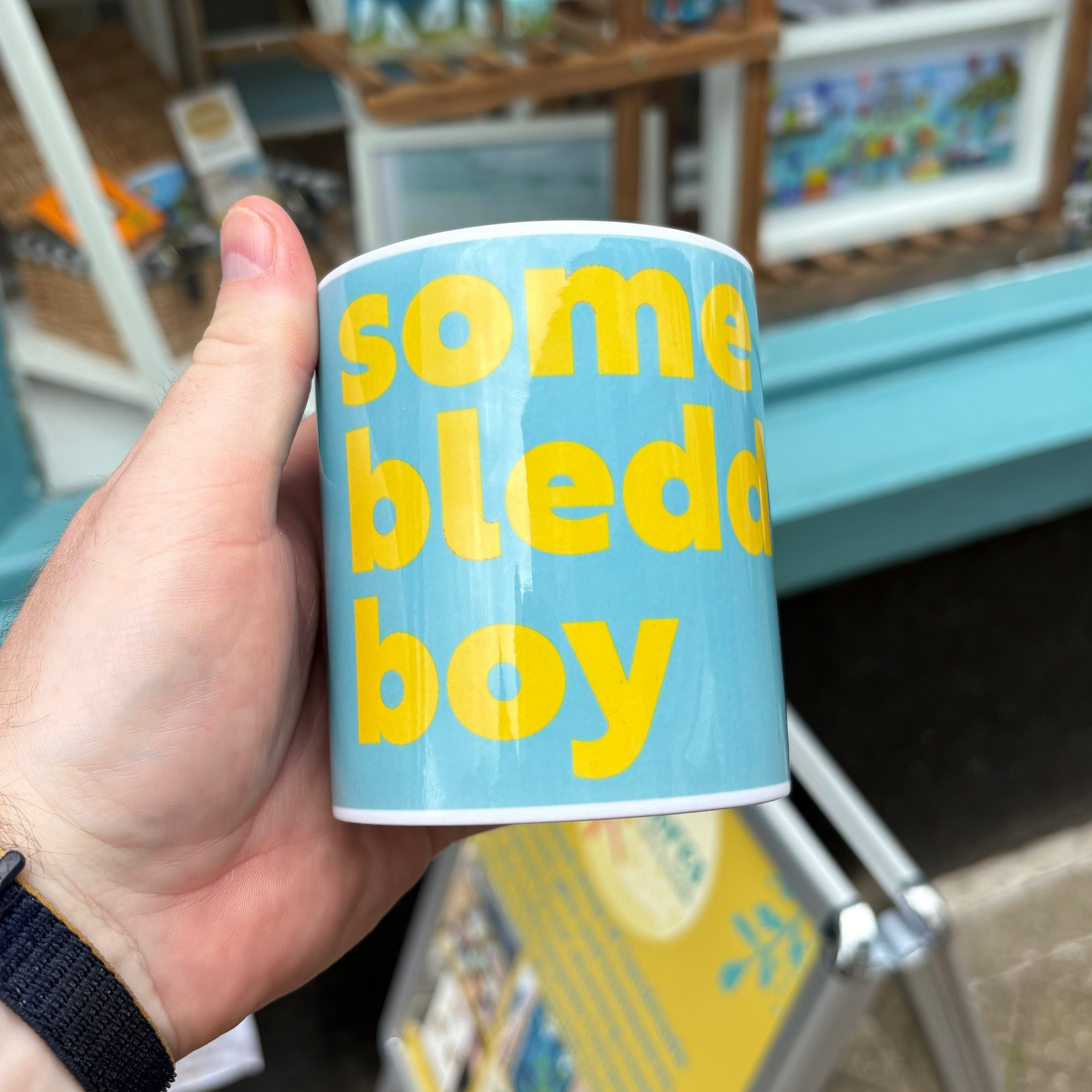 Hand holding a blue mug with yellow text in front of a store display.