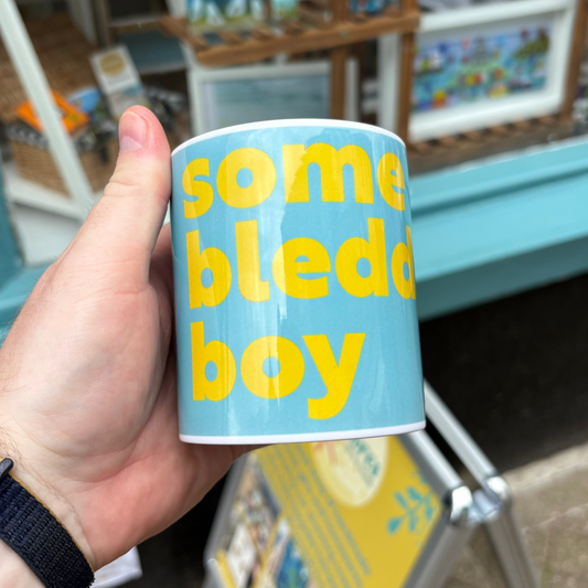 Hand holding a blue mug with yellow text in front of a store display.