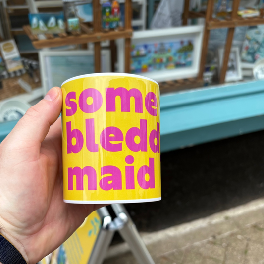 Hand holding a yellow mug with pink text in an outdoor setting