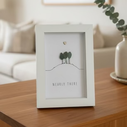 Framed artwork with trees and 'NEARLY THERE' text on a wooden surface